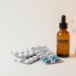Flacon de CBD à côté de plaquettes de médicaments et d'un verre d'eau, sur fond clair